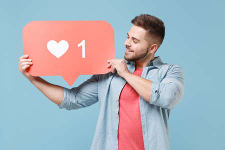 Smiling young bearded guy in casual shirt posing isolated on pastel blue background studio portrait. People lifestyle concept. Mock up copy space. Hold huge like sign from social network heart form.の写真素材