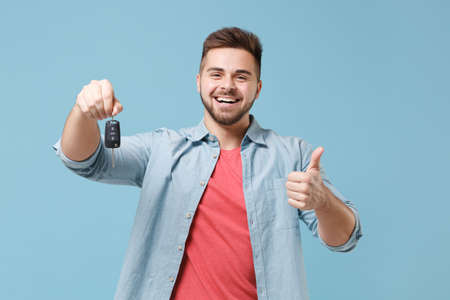 Laughing young bearded guy 20s in casual shirt posing isolated on pastel blue wall background studio portrait. People emotions lifestyle concept. Mock up copy space. Hold car keys, showing thumb up.の写真素材