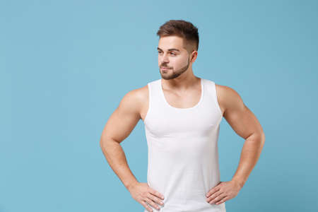 Attractive young bearded guy 20s in white singlet posing isolated on pastel blue background. Sport...