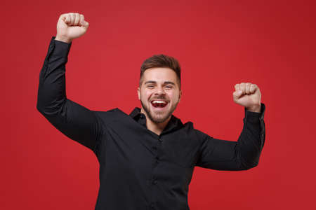 Joyful young bearded guy 20s in classic black shirt posing isolated on bright red background studio...