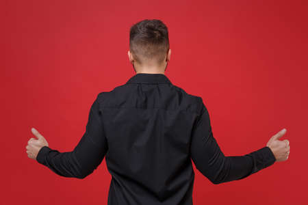 Back rear view of young guy 20s in classic black shirt posing isolated on bright red wall background...