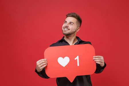 Pensive young bearded guy 20s in classic black shirt posing isolated on red background. People...
