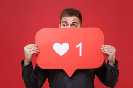 Funny young bearded guy 20s in classic black shirt posing isolated on red background. People...