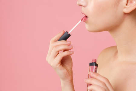 Close up cropped blonde half naked woman 20s perfect skin nude make up isolated on pastel pink wall background studio portrait. Skin care healthcare cosmetic procedures concept. Hold liquid lipstick.の写真素材