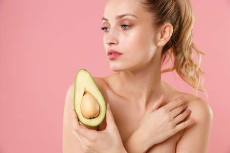 Close up half naked woman 20s perfect skin nude make up blue eyes hold in hand fresh ripe avocado isolated on pastel pink background studio portrait. Skin care healthcare cosmetic procedures concept.の写真素材