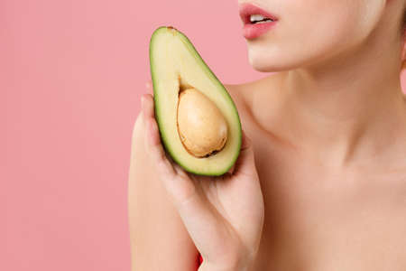 Close up cropped half naked woman 20s perfect skin nude make up hold in hand fresh ripe avocado...