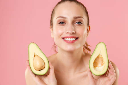 Close up half naked woman 20s perfect skin nude make up blue eyes hold in hand fresh ripe avocado...