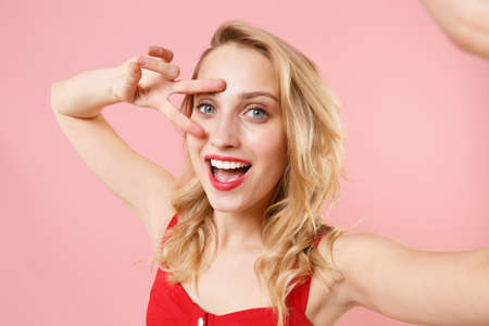 Close up of cheerful young woman in red sexy clothes posing isolated on pastel pink background....