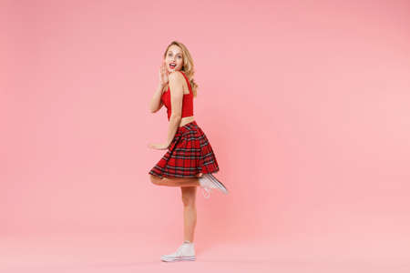 Side view of cheerful young blonde woman girl in red sexy clothes posing isolated on pastel pink...