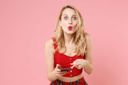 Amazed young blonde woman girl in red sexy clothes posing isolated on pastel pink background. People...
