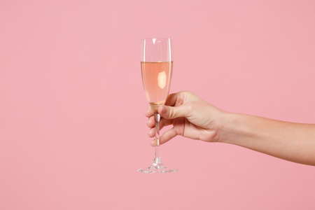 Close up cropped photo of female hold in hand glass of champagne isolated on pastel pink wall background. Copy space advertising mock up. Valentines Day Womens Day birthday holiday party concept.の写真素材