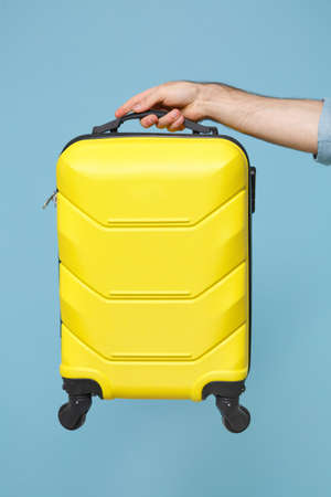 Close up cropped photo of male hold in hand yellow plastic suitcase baggage isolated on pastel blue background. Passenger traveling abroad on weekends. Air flight journey concept. Copy space mock up.の写真素材
