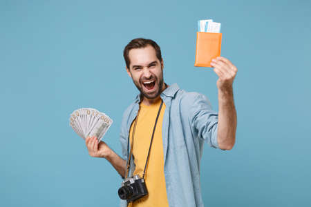 Happy traveler tourist man in yellow clothes with photo camera isolated on blue background. Passenger traveling on weekends. Air flight journey. Hold passport boarding pass tickets fan of cash money.の写真素材