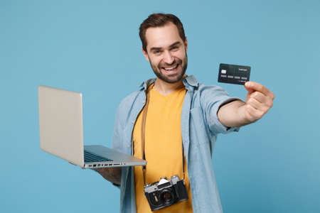 Smiling traveler tourist man in casual clothes with photo camera isolated on blue background. Passenger traveling on weekends. Air flight journey. Work on laptop booking hotel hold credit bank card.の写真素材