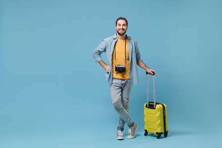 Smiling traveler tourist man in yellow summer casual clothes with photo camera isolated on blue...