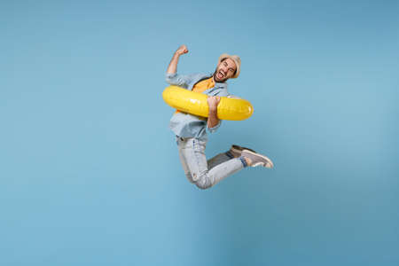 Happy traveler tourist man in yellow clothes isolated on blue background. Male passenger traveling abroad on weekends. Air flight journey concept. Jumping hold inflatable ring doing winner gesture.の写真素材