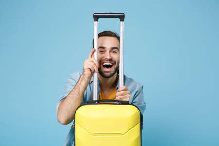 Laughing traveler tourist man in summer yellow casual clothes isolated on blue wall background. Male passenger traveling abroad to travel on weekend. Air flight journey concept. Sitting near suitcase.の写真素材