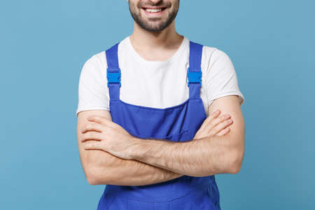 Cropped image of smiling young man in coveralls isolated on pastel blue background studio portrait. Instruments accessories for renovation apartment room. Repair home concept. Holding hands crossed.の写真素材