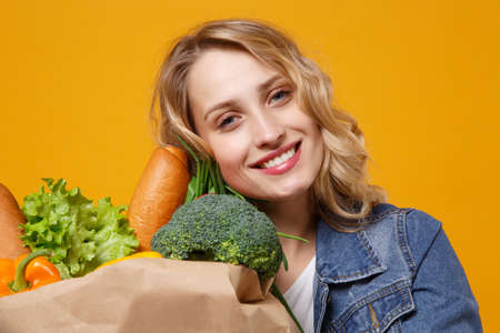 Close up of smiling young woman in denim clothes isolated on orange background. Delivery service...