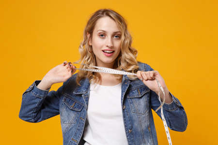 Beautiful young woman in denim clothes isolated on yellow orange wall background in studio. Proper...