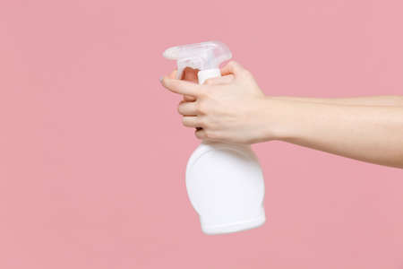 Close up cropped photo of female housewife hold in hands atomizer spray with washing cleanser isolated on pastel pink wall background in studio. Copy space advertising mock up. Housekeeping concept.の写真素材