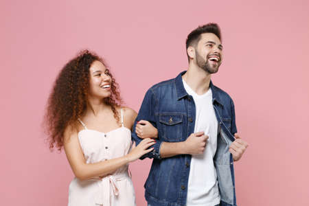 Cheerful young couple friends european guy african american girl in casual clothes isolated on pastel pink background. People lifestyle concept. Mock up copy space. Looking aside holding hands folded.の写真素材