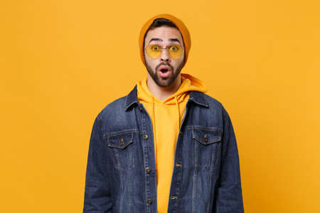 Shocked young hipster guy in fashion jeans denim clothes posing isolated on yellow orange background studio portrait. People sincere emotions lifestyle concept. Mock up copy space. Keeping mouth open.の写真素材