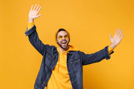 Happy young hipster guy in fashion jeans denim clothes posing isolated on yellow orange background...