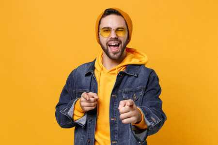 Funny young hipster guy in fashion jeans denim clothes posing isolated on yellow orange background...