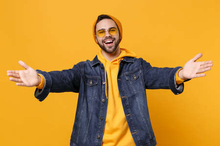 Pleasant young hipster guy in fashion jeans denim clothes posing isolated on yellow orange background studio portrait. People lifestyle concept. Mock up copy space. Standing with outstretched hands.の写真素材