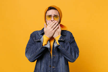 Shocked young hipster guy in fashion jeans denim clothes posing isolated on yellow orange wall...