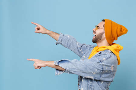 Side view of funny young hipster guy in fashion jeans denim clothes posing isolated on pastel blue...