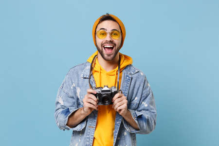 Excited young hipster guy in fashion jeans denim clothes posing isolated on pastel blue wall background studio portrait. People lifestyle concept. Mock up copy space. Hold retro vintage photo camera.の写真素材