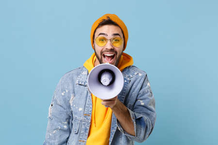 Excited crazy young hipster guy in fashion jeans denim clothes posing isolated on pastel blue...