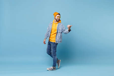 Cheerful young hipster guy in fashion jeans denim clothes posing isolated on pastel blue wall...