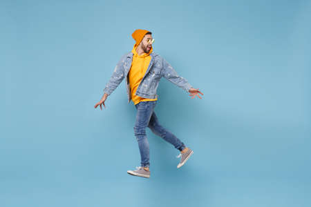 Side view of excited young hipster guy in fashion jeans denim clothes posing isolated on pastel blue...