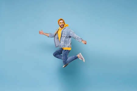 Side view of funny young hipster guy in fashion jeans denim clothes posing isolated on pastel blue background. People lifestyle concept. Mock up copy space. Jumping, spreading hands, looking aside.の写真素材