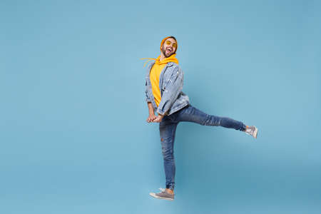 Funny young hipster guy in fashion jeans denim clothes posing isolated on pastel blue wall...
