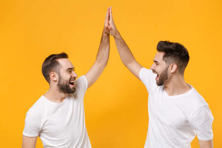 Funny young men guys friends in white blank empty t-shirts posing isolated on yellow orange...
