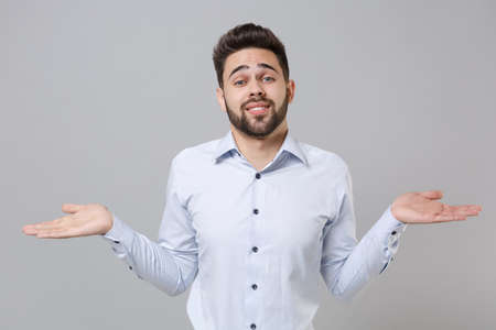 Perplexed bewildered young unshaven business man in light shirt posing isolated on grey background studio portrait. Achievement career wealth business concept. Mock up copy space. Spreading hands.の写真素材