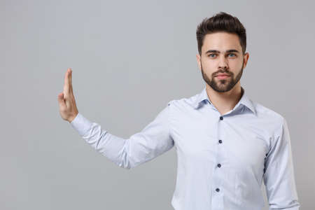 Serious young unshaven business man in light shirt posing isolated on grey background in studio. Achievement career wealth business concept. Mock up copy space. Showing stop gesture aside with palm.の写真素材