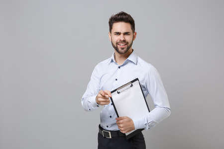 Perplexed young business man in light shirt isolated on grey background. Achievement career wealth business concept. Hold clipboard with blank empty sheet workspace, pointing index finger on camera.の写真素材