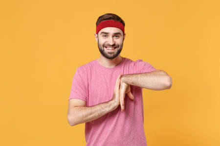 Smiling young bearded fitness sporty guy sportsman in headband t-shirt spend weekend in home gym isolated on yellow background. Workout sport motivation concept. Doing stretching exercising for hands.の写真素材