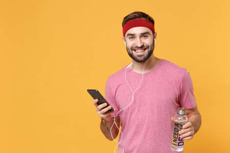 Smiling fitness sporty guy 20s sportsman in headband t-shirt in home gym isolated on yellow...
