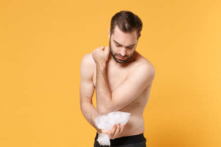Young bearded fitness sporty guy 20s  sportsman in home gym isolated on yellow wall background. Workout sport motivation lifestyle concept. Get injured hold ice pack cooling down arm elbow pain.の写真素材