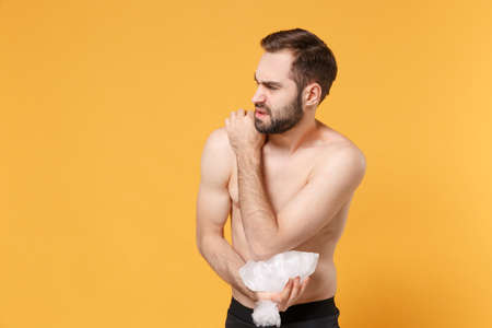 Displeased young bearded fitness sporty guy 20s  sportsman in home gym isolated on yellow wall background. Workout sport motivation concept. Get injured hold ice pack cooling down arm elbow pain.の写真素材