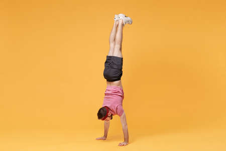 Young bearded fitness sporty guy 20s sportsman in headband t-shirt spend weekend in home gym isolated on yellow background in studio. Workout sport motivation lifestyle concept. Standing on hands.の写真素材