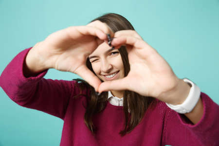 Young woman girl in casual clothes posing isolated on blue background studio portrait. People sincere emotions lifestyle concept. Mock up copy space. showing look through shape heart with hands,の写真素材