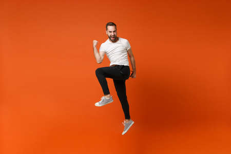 Happy joyful young man in casual white t-shirt posing isolated on bright orange wall background...