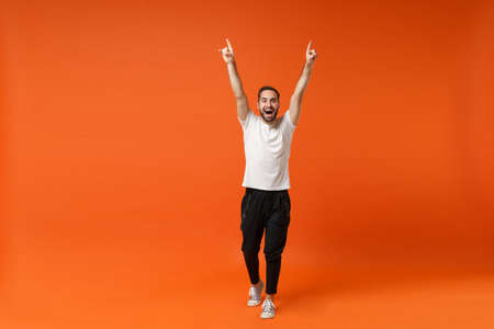 Funny young man in casual white t-shirt posing isolated on orange background, studio portrait. .